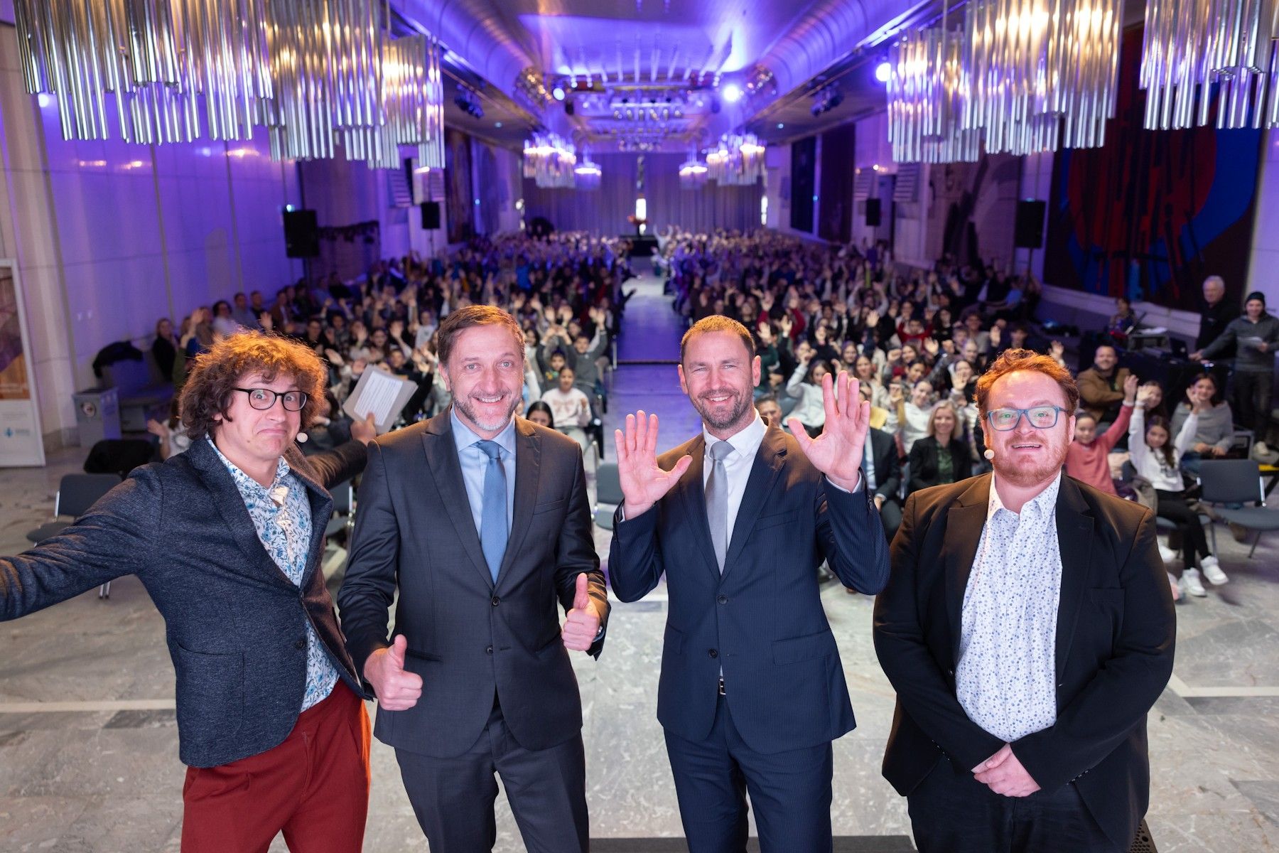 Rok Škrlep, Klemen Boštijančič, Primož dolenc in Juš milčinski stojijo pred polno dvorano otrok kot bi delali selfie