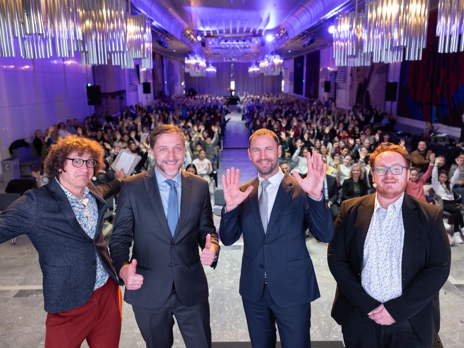 Rok Škrlep, Klemen Boštijančič, Primož dolenc in Juš milčinski stojijo pred polno dvorano otrok kot bi delali selfie