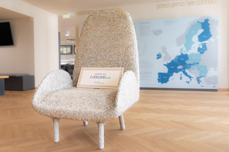 An armchair made of shredded euro banknotes with a sign on the seat reading “SEDIM NA 2.000.000 EUR,” which means "I am sitting on 2.000.000 euros" and a map of Europe on the wall behind.