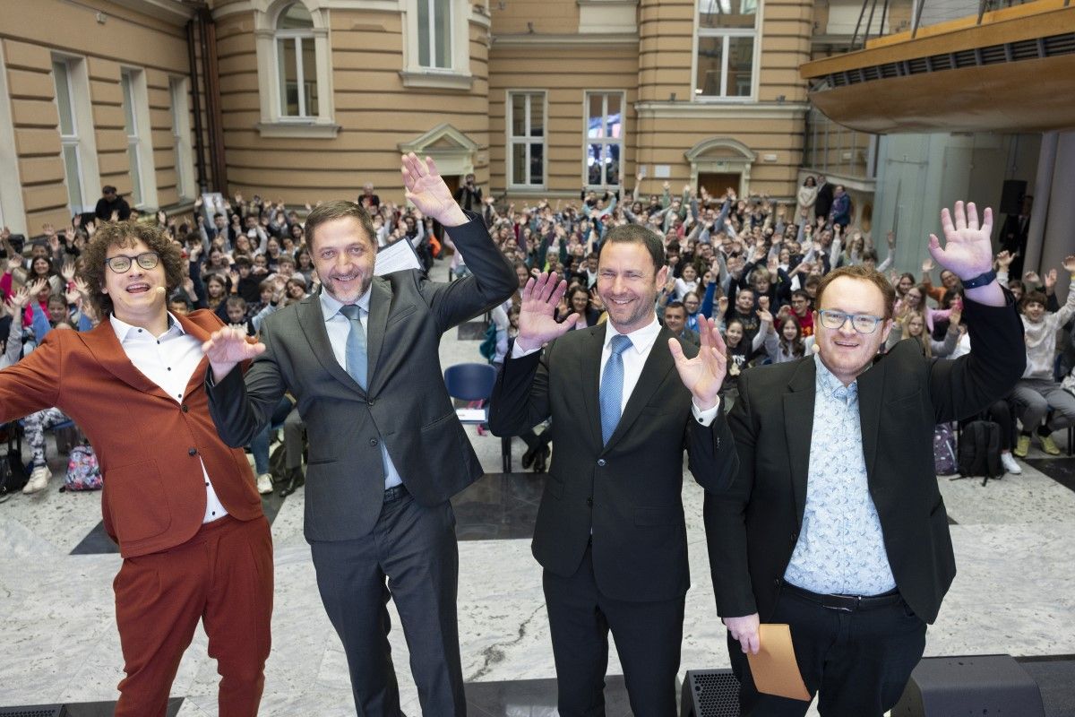 Minister Klemen Boštjančič, Deputy Governor Primož Dolenc, Juš and Rok on stage in front of a full hall of children