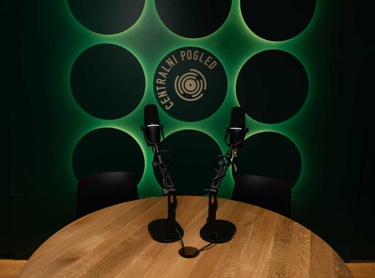 v ospredju miza z dvema mikrofonoma, v ozadju napis Centralni pogled na ozzadju z zelenimi krogi