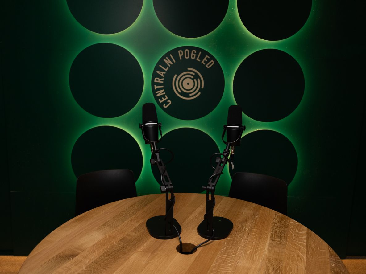 v ospredju miza z dvema mikrofonoma, v ozadju napis Centralni pogled na ozzadju z zelenimi krogi